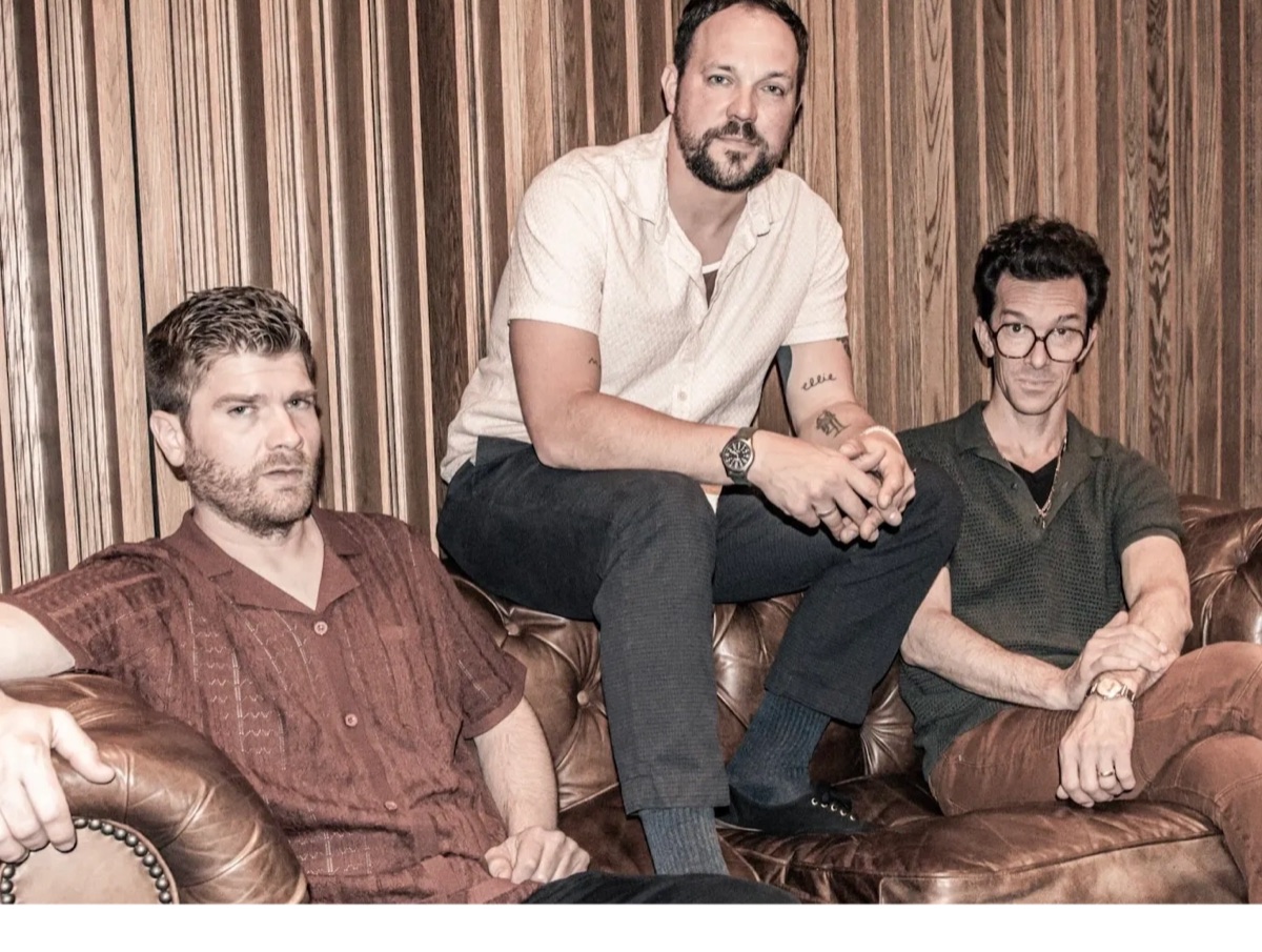 Pressing Strings — the trio on a brown leather Chesterfield in front of a wood-slat wall